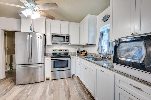 kitchen with white cabinetry, stainless steel appliances, a sink, stone counters, and light wood finished floors