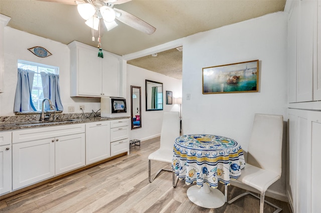 kitchen with stone counters, a sink, light wood-type flooring, white cabinets, and ceiling fan