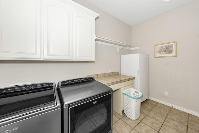 washroom featuring light tile patterned floors, cabinet space, washing machine and clothes dryer, and baseboards