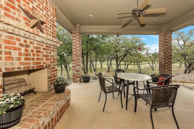 view of patio with an outdoor brick fireplace, outdoor dining space, and ceiling fan
