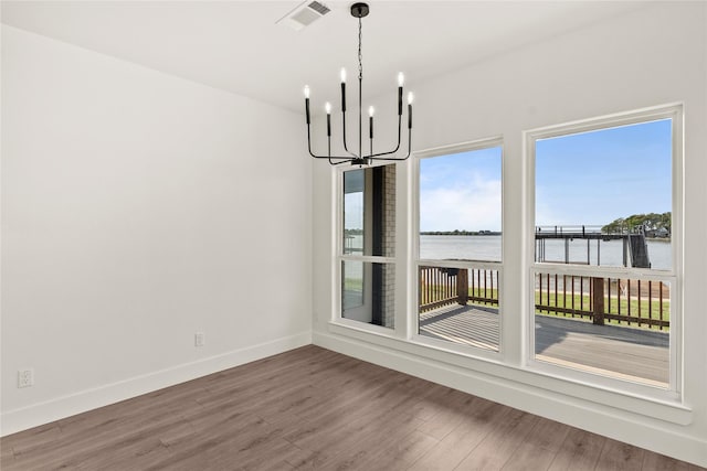 unfurnished dining area with a water view, baseboards, visible vents, a notable chandelier, and wood finished floors