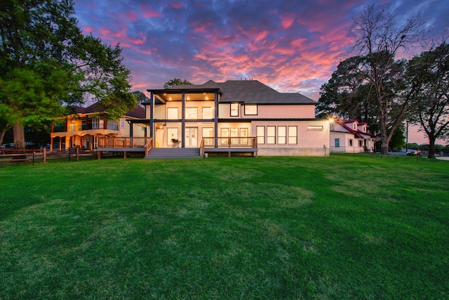 back of house at dusk featuring a lawn, fence, and a deck