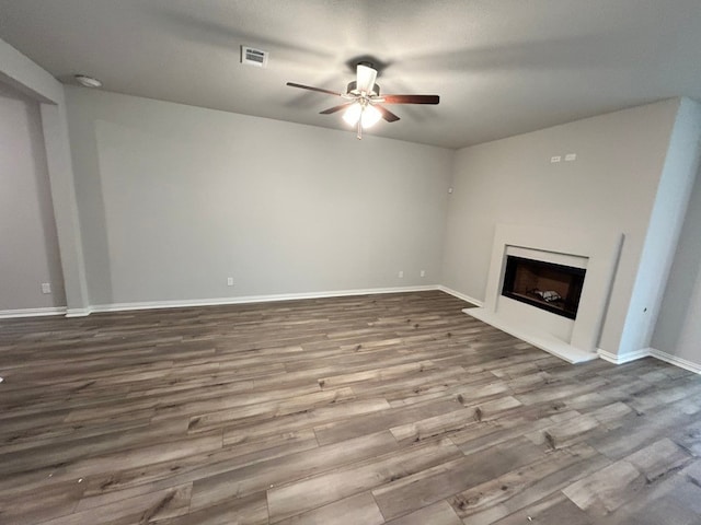 unfurnished living room featuring baseboards, a fireplace with raised hearth, a ceiling fan, and wood finished floors