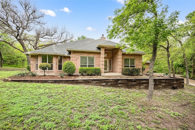 view of front of property with roof with shingles, a chimney, a front lawn, and brick siding