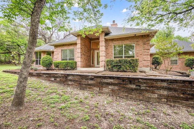 rear view of property featuring a patio, a chimney, a shingled roof, and brick siding
