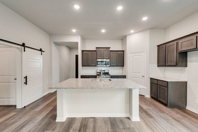 3523 Columbus St, Gainesville, TX 76240 - kitchen featuring appliances with stainless steel finishes, a barn door, dark brown cabinetry, light wood finished floors, and recessed lighting