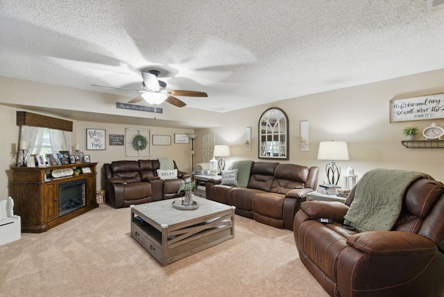 living room featuring a textured ceiling, a fireplace, ceiling fan, and light colored carpet