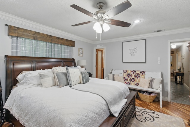 bedroom with wood finished floors, a textured ceiling, visible vents, baseboards, and ornamental molding