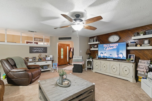 living area with wood walls, a textured ceiling, a ceiling fan, and visible vents