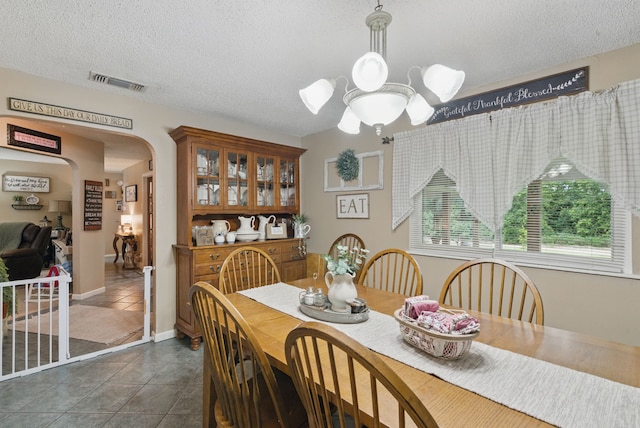 dining room featuring a textured ceiling, dark tile patterned floors, visible vents, arched walkways, and a notable chandelier
