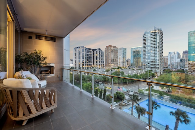 balcony at dusk with exterior fireplace and a city view