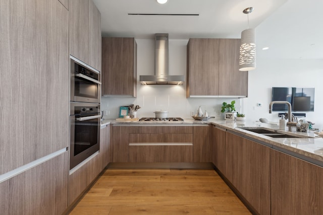 kitchen with a sink, wall chimney range hood, modern cabinets, and light stone countertops