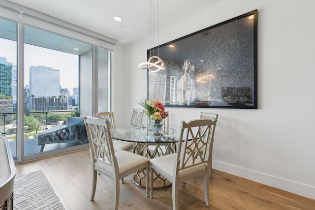 dining area with a city view, wood finished floors, baseboards, and a wall of windows