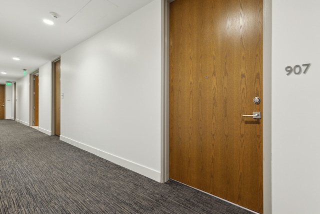 hallway featuring baseboards and dark carpet