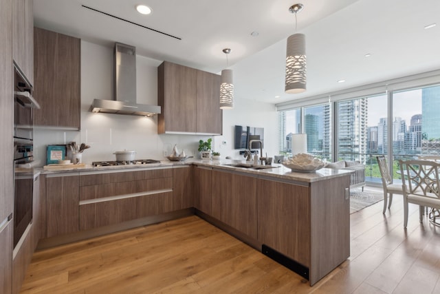 kitchen with wall chimney exhaust hood, modern cabinets, light wood-style flooring, a peninsula, and stainless steel gas stovetop