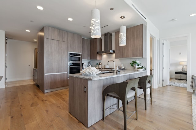 kitchen with wall chimney range hood, a breakfast bar, modern cabinets, and light wood-style flooring
