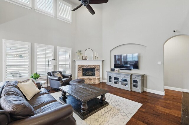 living room with a brick fireplace, baseboards, wood finished floors, a ceiling fan, and arched walkways