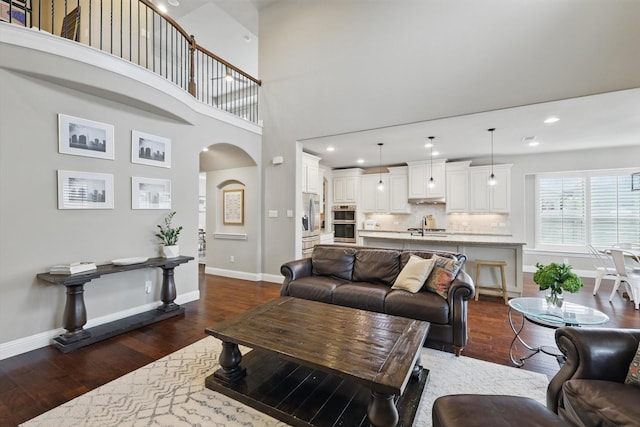 living room with baseboards, recessed lighting, dark wood finished floors, arched walkways, and a high ceiling