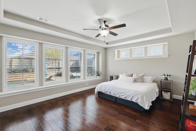 bedroom featuring a tray ceiling, baseboards, visible vents, and wood-type flooring