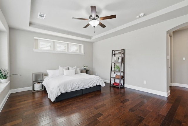 bedroom featuring hardwood / wood-style floors, baseboards, a raised ceiling, arched walkways, and visible vents