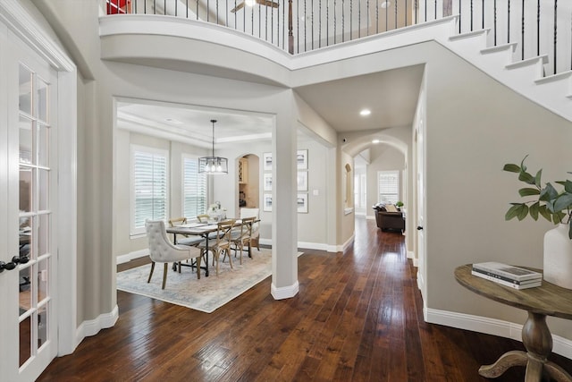 foyer with dark wood-style floors, arched walkways, and baseboards