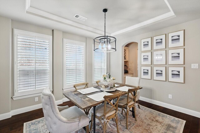 dining space featuring arched walkways, a tray ceiling, visible vents, and dark wood-type flooring