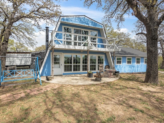 rear view of property with a fire pit, a gambrel roof, a balcony, a patio, and a yard