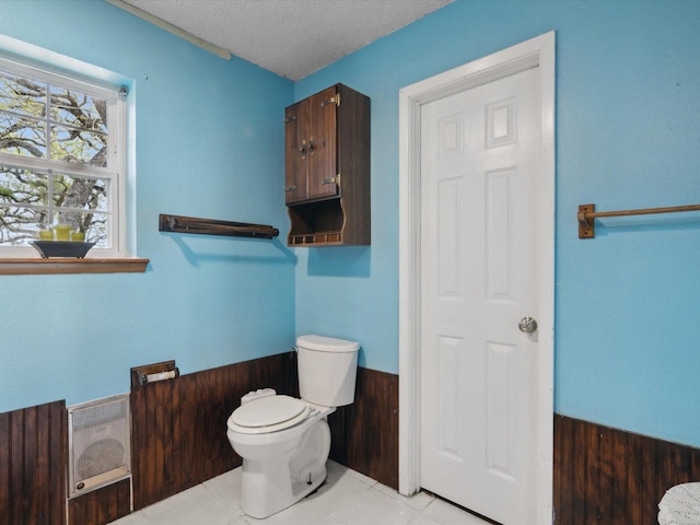 bathroom with a textured ceiling, toilet, and tile patterned flooring