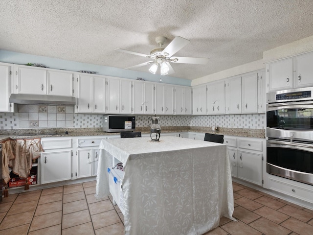 kitchen featuring decorative backsplash, under cabinet range hood, stainless steel appliances, and light tile patterned floors