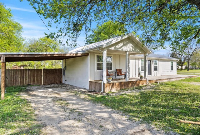 view of front of home featuring a front lawn, a carport, fence, and dirt driveway