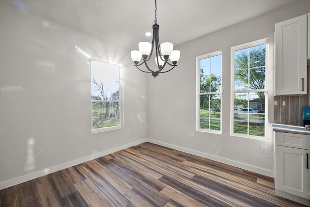 unfurnished dining area with a chandelier, baseboards, and dark wood finished floors