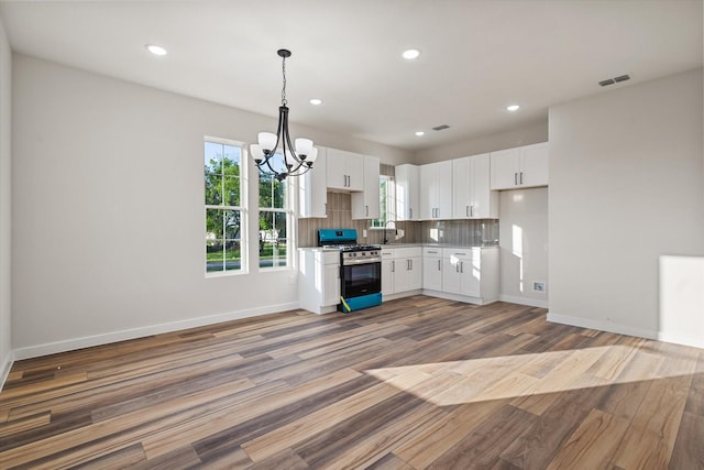 kitchen with stainless steel range with gas cooktop, a chandelier, wood finished floors, white cabinets, and recessed lighting
