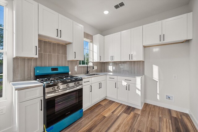 kitchen featuring stainless steel gas stove, a sink, light wood finished floors, light countertops, and backsplash