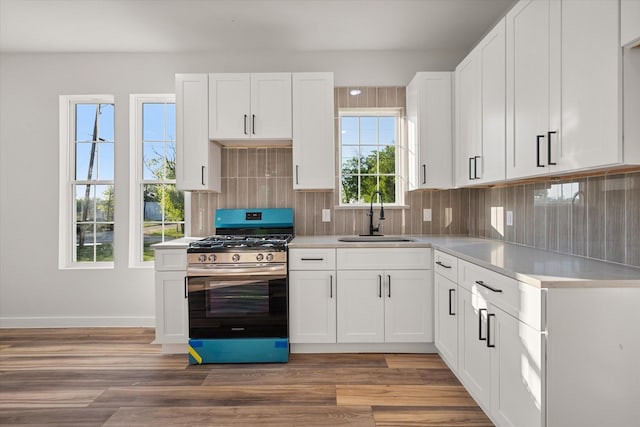 kitchen with stainless steel gas range, a sink, backsplash, light countertops, and white cabinetry