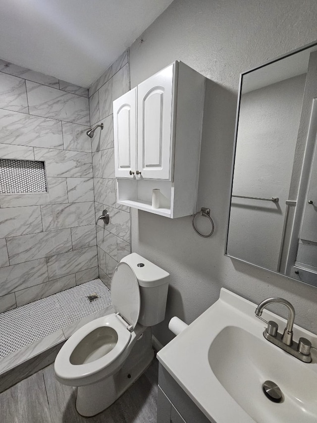 full bath with toilet, a tile shower, wood finished floors, vanity, and a textured wall
