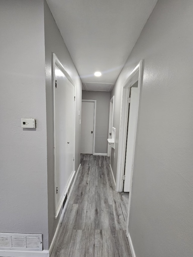 hallway with attic access, baseboards, visible vents, and wood finished floors