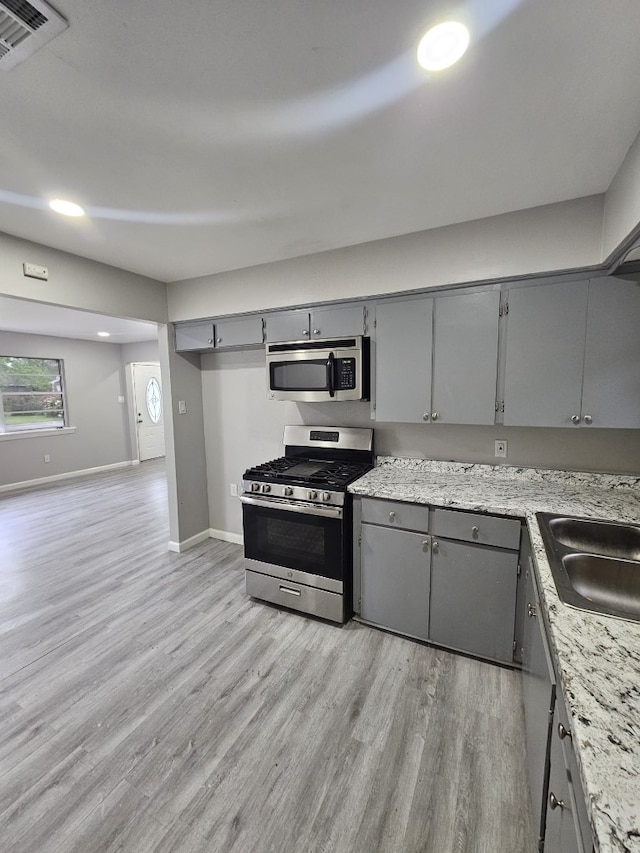 kitchen with a sink, appliances with stainless steel finishes, gray cabinetry, baseboards, and light wood-style floors