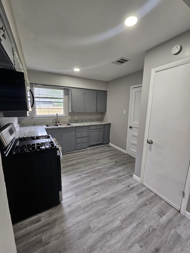 kitchen with gray cabinetry, light wood-style flooring, visible vents, and gas range oven