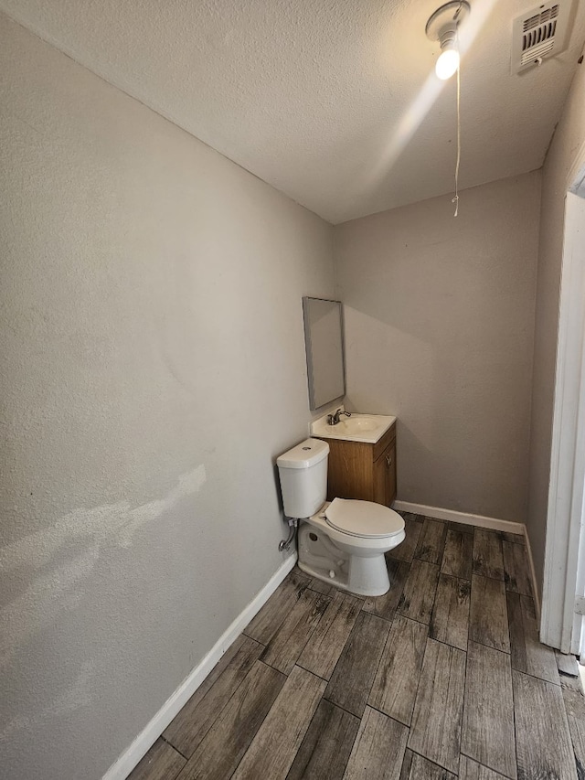 bathroom featuring wood finish floors, toilet, baseboards, a textured ceiling, and visible vents