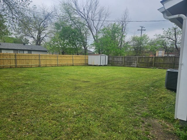 view of yard featuring central AC unit, a fenced backyard, an outdoor structure, and a shed