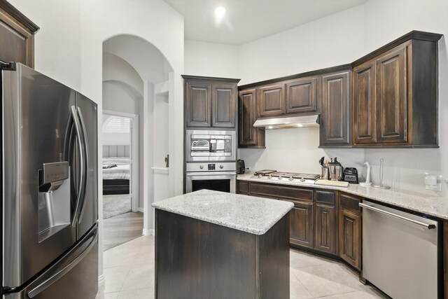 1125 Overton St, Frisco, TX 75036 - kitchen with appliances with stainless steel finishes, under cabinet range hood, dark brown cabinetry, a kitchen island, and light tile patterned floors