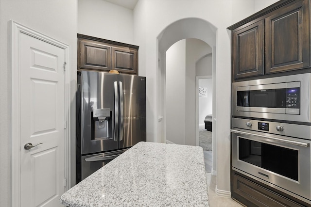 1125 Overton St, Frisco, TX 75036 - kitchen featuring stainless steel appliances, arched walkways, dark brown cabinets, and light stone counters