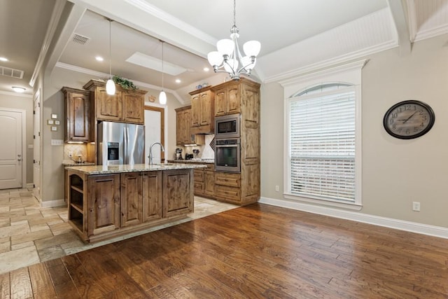 kitchen featuring light stone counters, a sink, stainless steel appliances, a center island with sink, and visible vents