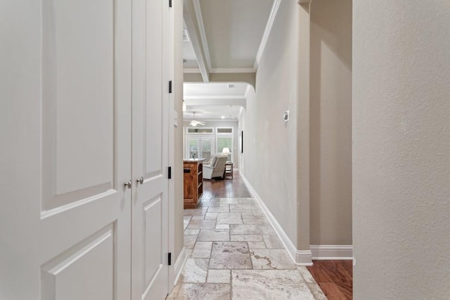 hall featuring stone tile flooring, a textured wall, baseboards, and ornamental molding