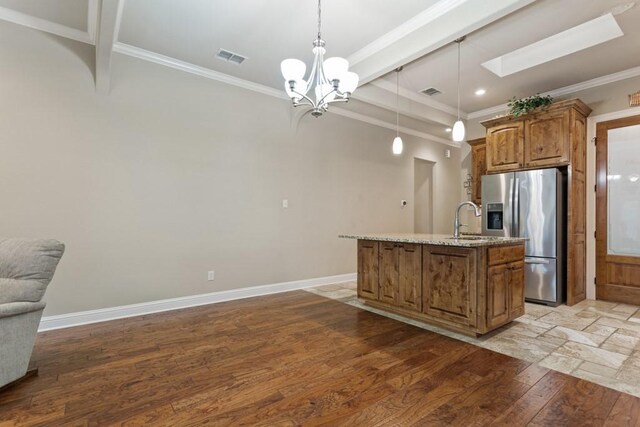 kitchen with a kitchen island with sink, stainless steel fridge, light wood-type flooring, brown cabinetry, and ornamental molding