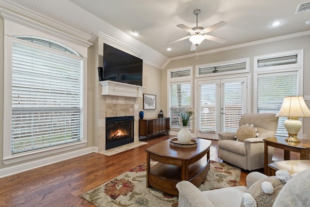 living room with wood finished floors, visible vents, a ceiling fan, crown molding, and a fireplace