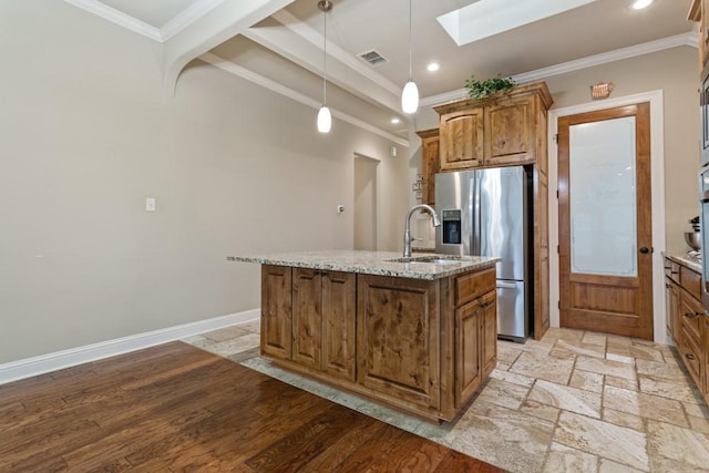 kitchen with a kitchen island with sink, a sink, a skylight, stainless steel fridge with ice dispenser, and ornamental molding