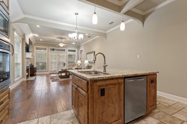 kitchen featuring a sink, a center island with sink, open floor plan, light stone countertops, and brown cabinetry