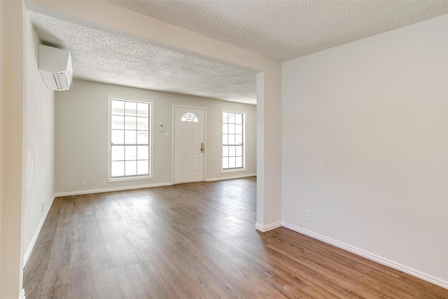 entrance foyer with baseboards, a wall mounted air conditioner, a textured ceiling, and wood finished floors
