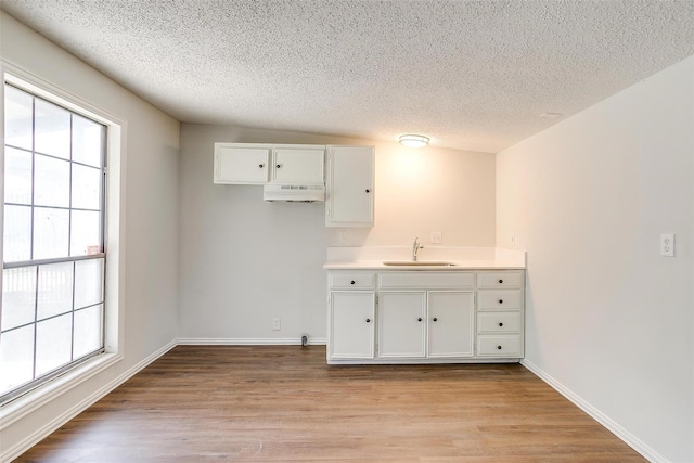 kitchen with baseboards, a textured ceiling, a sink, light wood-style floors, and white cabinets